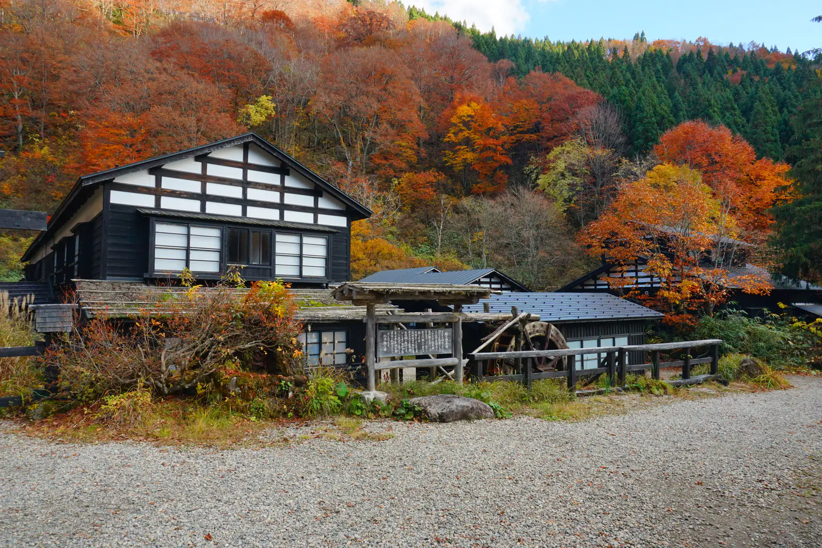 A black-timbered traditional onsen inn beneath a hillside blazing with red and orange autumn leaves