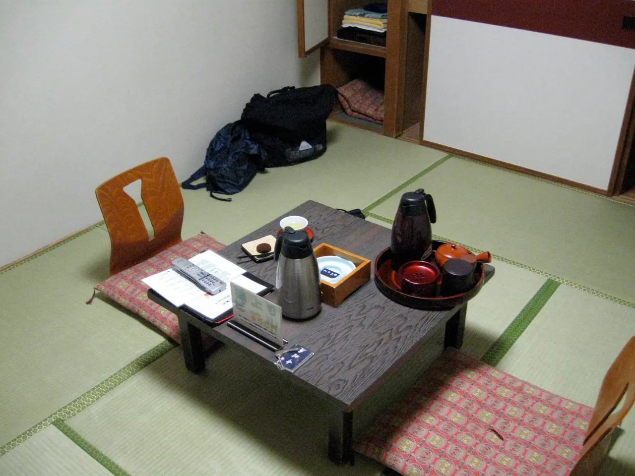 A tatami-floored ryokan room with a low lacquered table, tea set, thermos and floor chairs