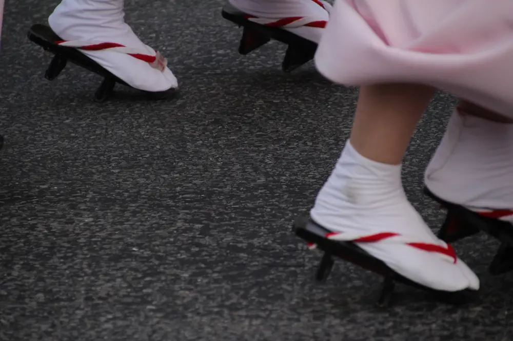 Close-up of dancers’ feet in white tabi socks and black wooden geta with red thongs