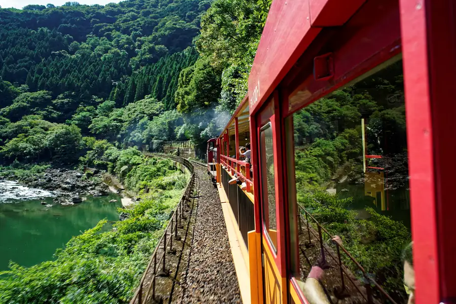 View from the open, red-framed Sagano Romantic Train down into the green Hozu River gorge