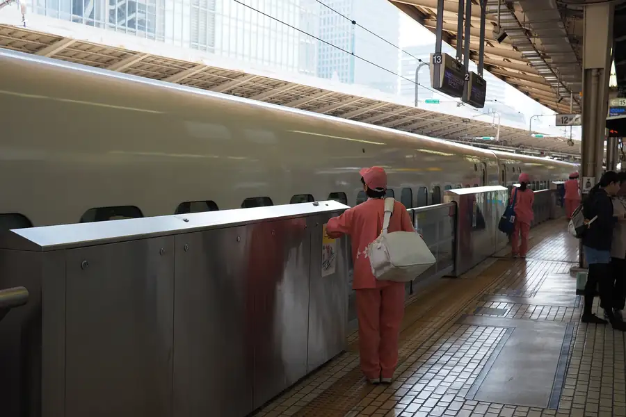Shinkansen cleaning staff in uniform waiting in a line on the platform as a train arrives