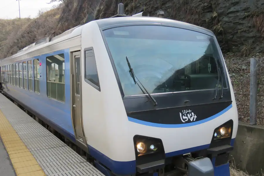 The blue and white Resort Shirakami Aoike train with large windows waiting at Senjōjiki Station